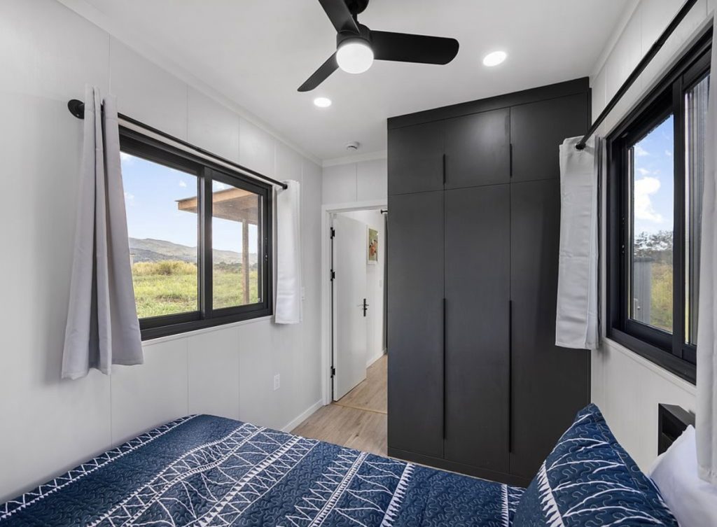Bedroom with navy bedding, a black wardrobe and a window onto green hills