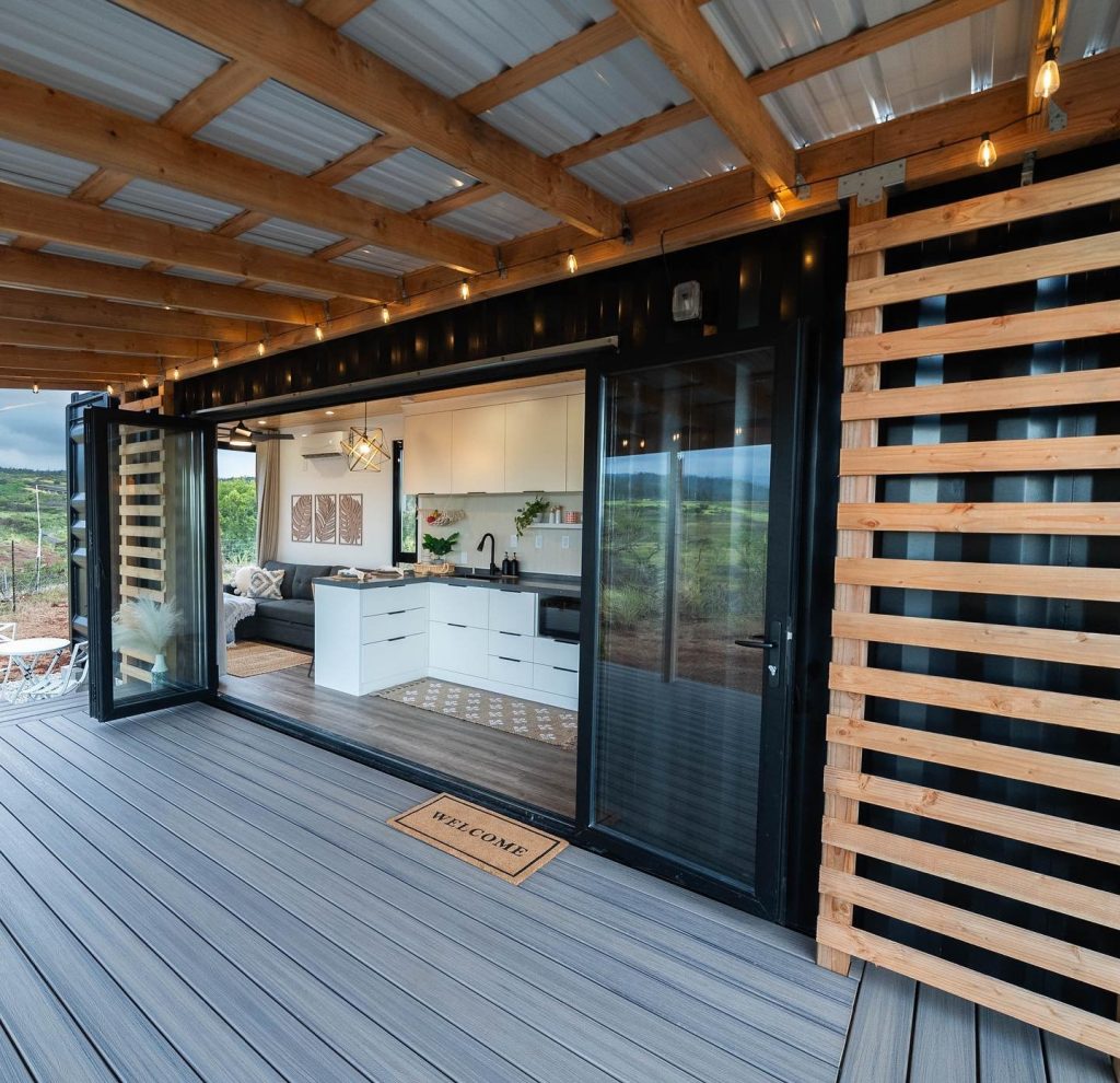 Covered deck with open glass folding doors leading into a white kitchen and living area