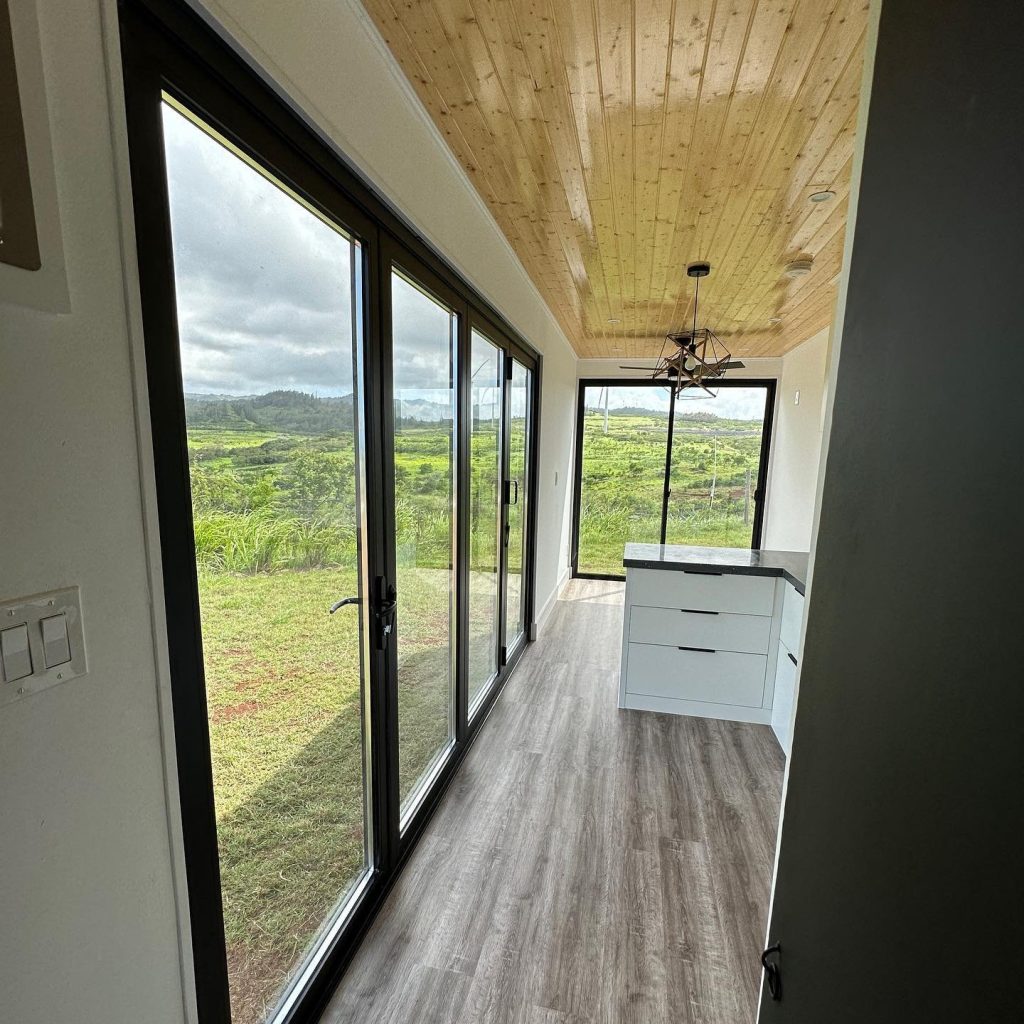 Wall of black-framed glass doors looking out over green hills, beneath a wood ceiling