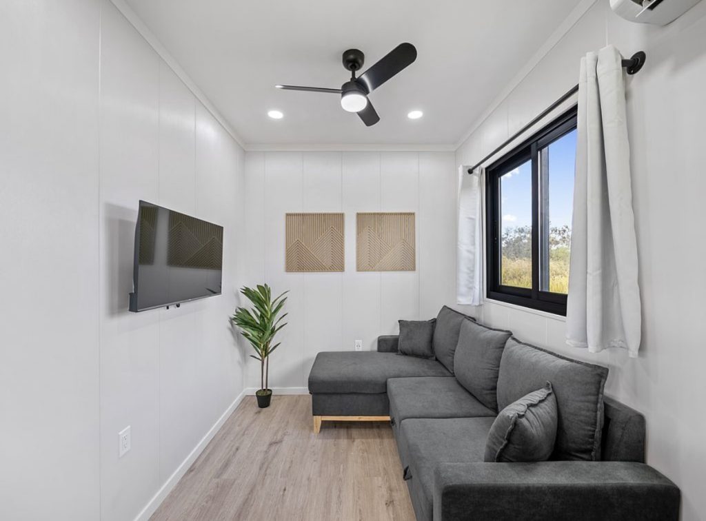 Living room with a grey sectional, wall-mounted TV and a black-framed window