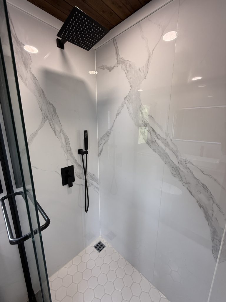 Walk-in shower with marble-look panels, black fixtures and hexagon floor tile